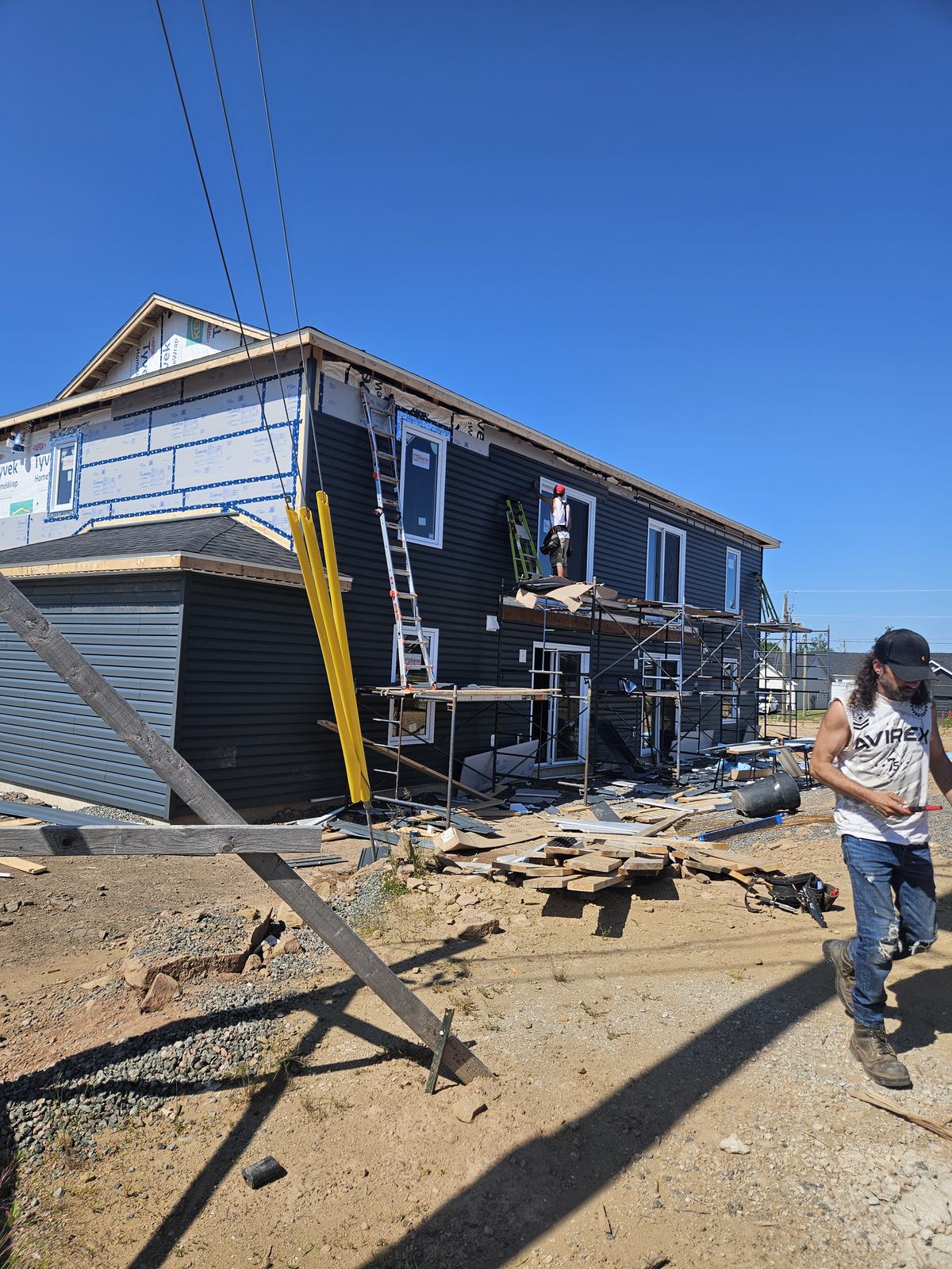 Workers installing dark vinyl siding on a two-storey residential home under construction with scaffolding in place.