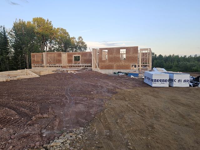 Brick residential home in early framing stage with wood walls and roof structure under construction.
