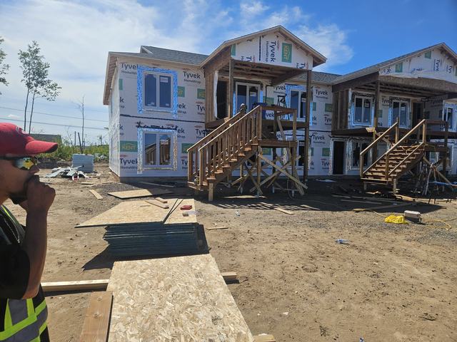 Multi-unit residential homes under construction with wood framing, sheathing, and exterior stairs installed.