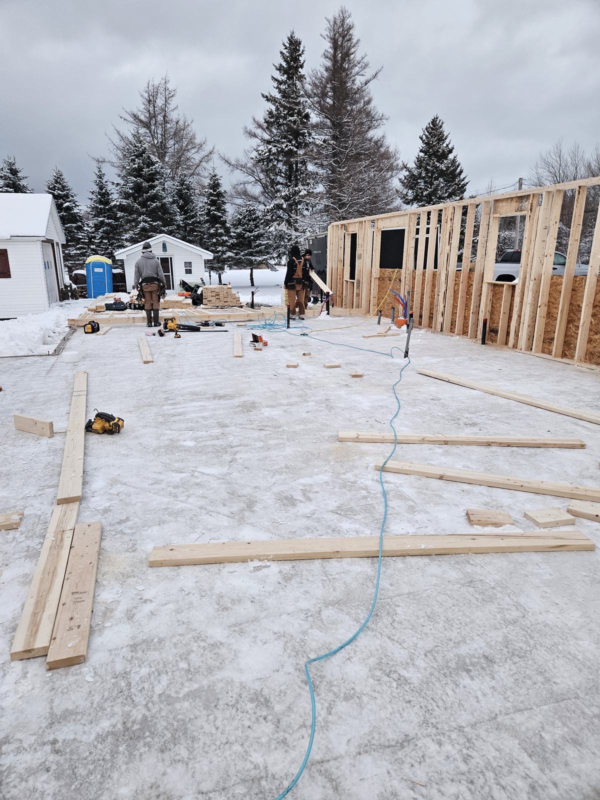 Wooden framing walls under construction on a residential home foundation in winter conditions.