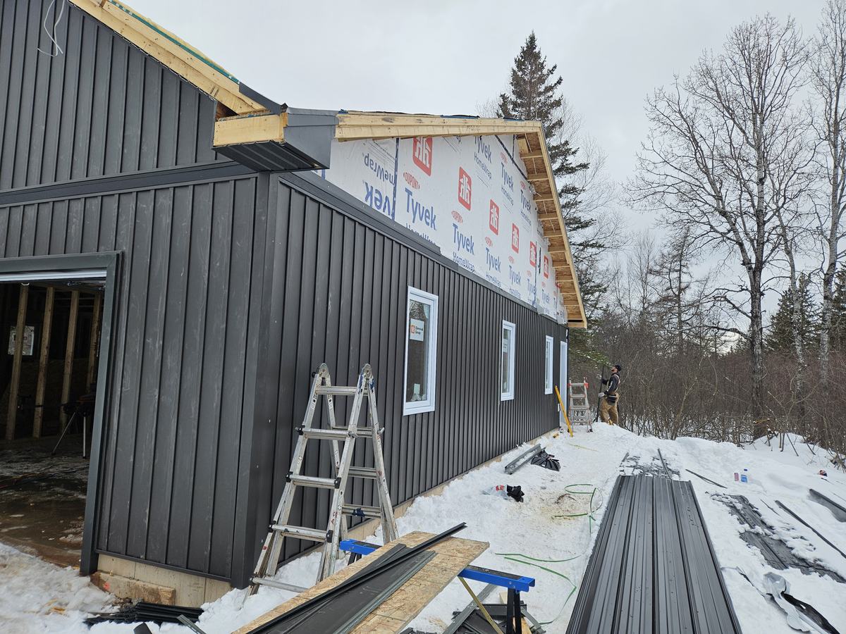 House under construction with Tyvek weather barrier applied to walls and Exterior siding being installed.