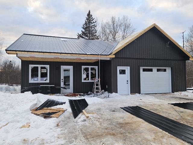 New residential construction featuring black metal siding, metal roofing, and attached garage in winter.