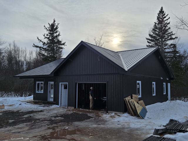 Newly framed residential home with metal roofing and vertical siding during final construction stages.