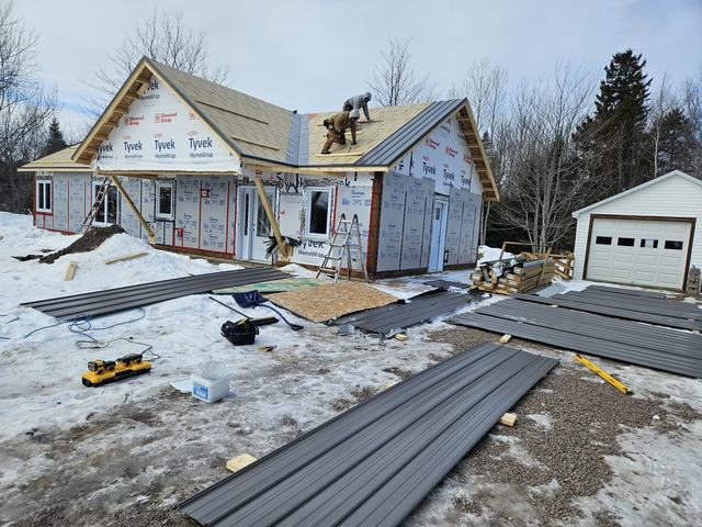 Workers installing metal roofing on a new residential home under construction.